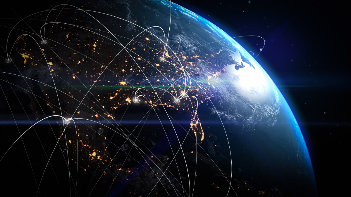 View of Earth from space at night showing illuminated city lights and glowing data network lines connecting various points across continents, symbolizing global communication, technology, and interconnected digital infrastructure.